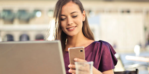Photo of a young woman smiling while looking at her mobile phone